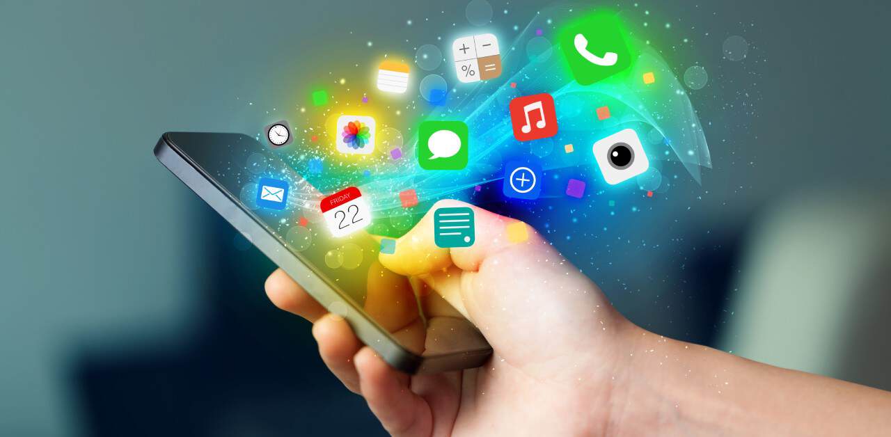 A hand holds a smartphone as colorful artificial intelligence app icons float out of the screen.