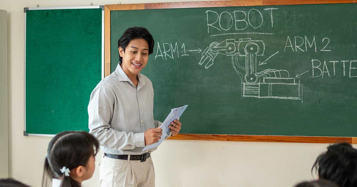 A teacher stands by a chalkboard with an AI-powered robotic arm diagram and labels, holding papers and addressing students seated at desks.