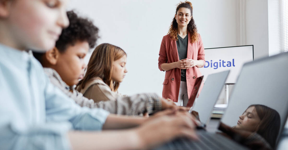 A teacher stands in front of a screen while several students work on laptops in a classroom, discussing the importance of managing your digital footprint.