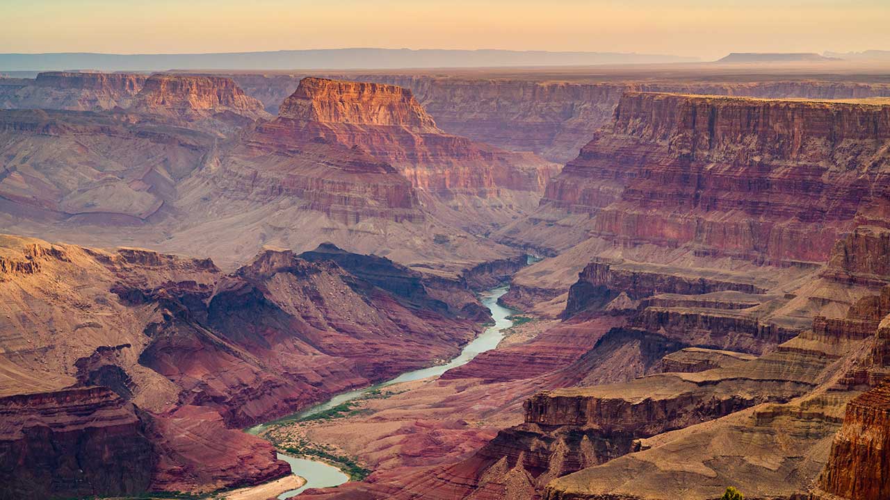 A wide view of the Grand Canyon at sunset, showing layered rock formations and the Colorado River winding through the canyon floor—capturing the awe of a perfect Dorm trip before heading to a Diamond Back game.