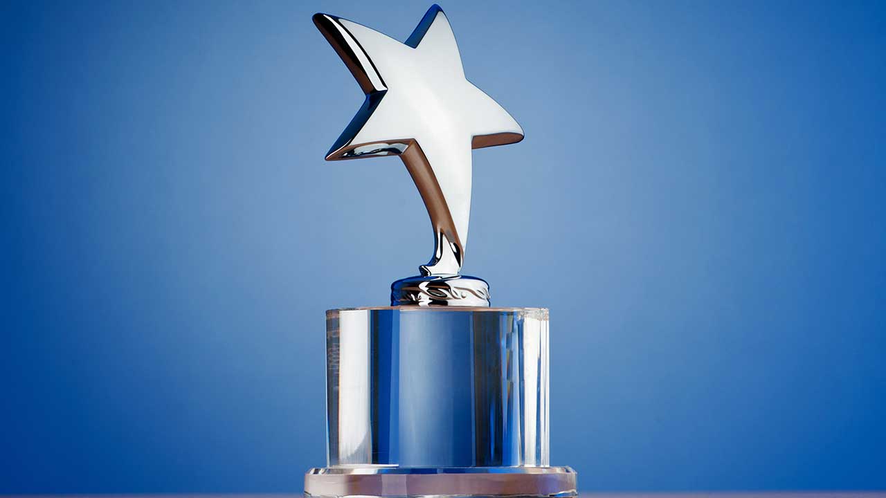 A silver star-shaped trophy sits on a clear cylindrical base against a plain blue background, ready to shine at the 4th Quarter Awards ceremony.