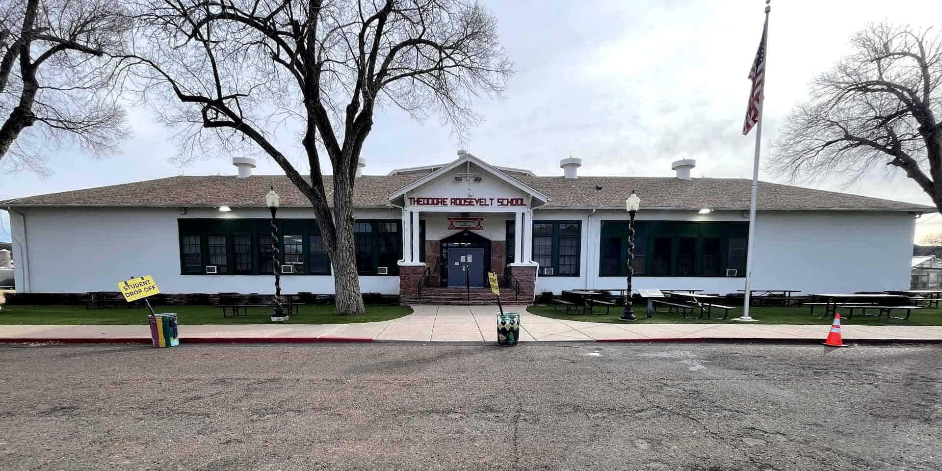 A single-story building labeled “Mohave Museum of History and Arts” with a flagpole, benches, picnic tables, and two leafless trees in front.