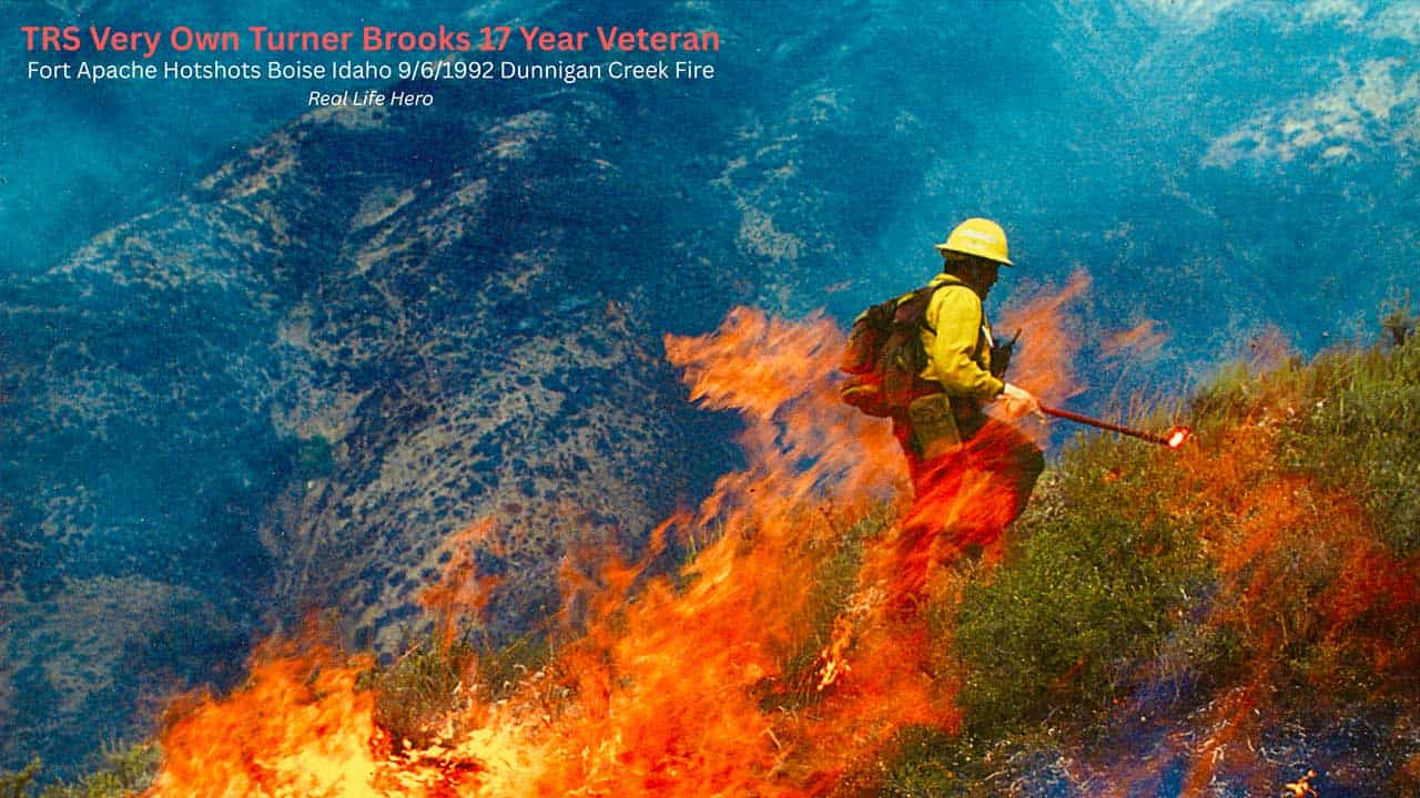 A firefighter in yellow gear uses a tool to control a brush fire on a hillside with mountains in the background. Text in the image honors Turner Brooks, a veteran firefighter.