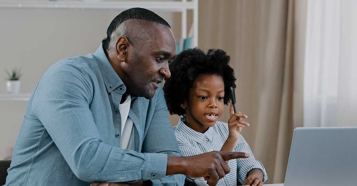 An adult and a child sit together at a desk, looking at a laptop screen. The adult is pointing at the screen while the child holds a pen, exploring AI tools to enhance their learning experience.