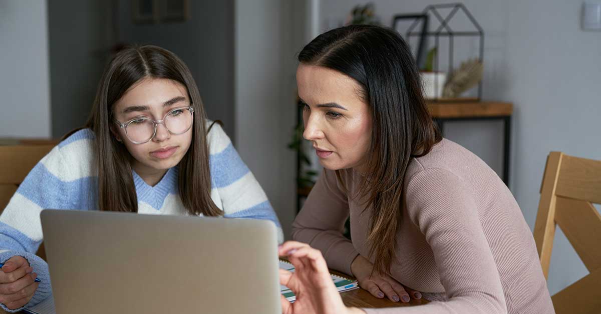 Two people sit at a table looking intently at a laptop screen, appearing focused and engaged in a discussion about financial sextortion.