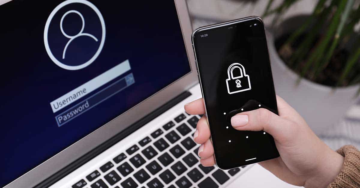 A person holds a smartphone with a lock icon on the screen next to a laptop displaying a login page requiring a username and password, illustrating the use of two-factor authentication (2FA) for enhanced security.